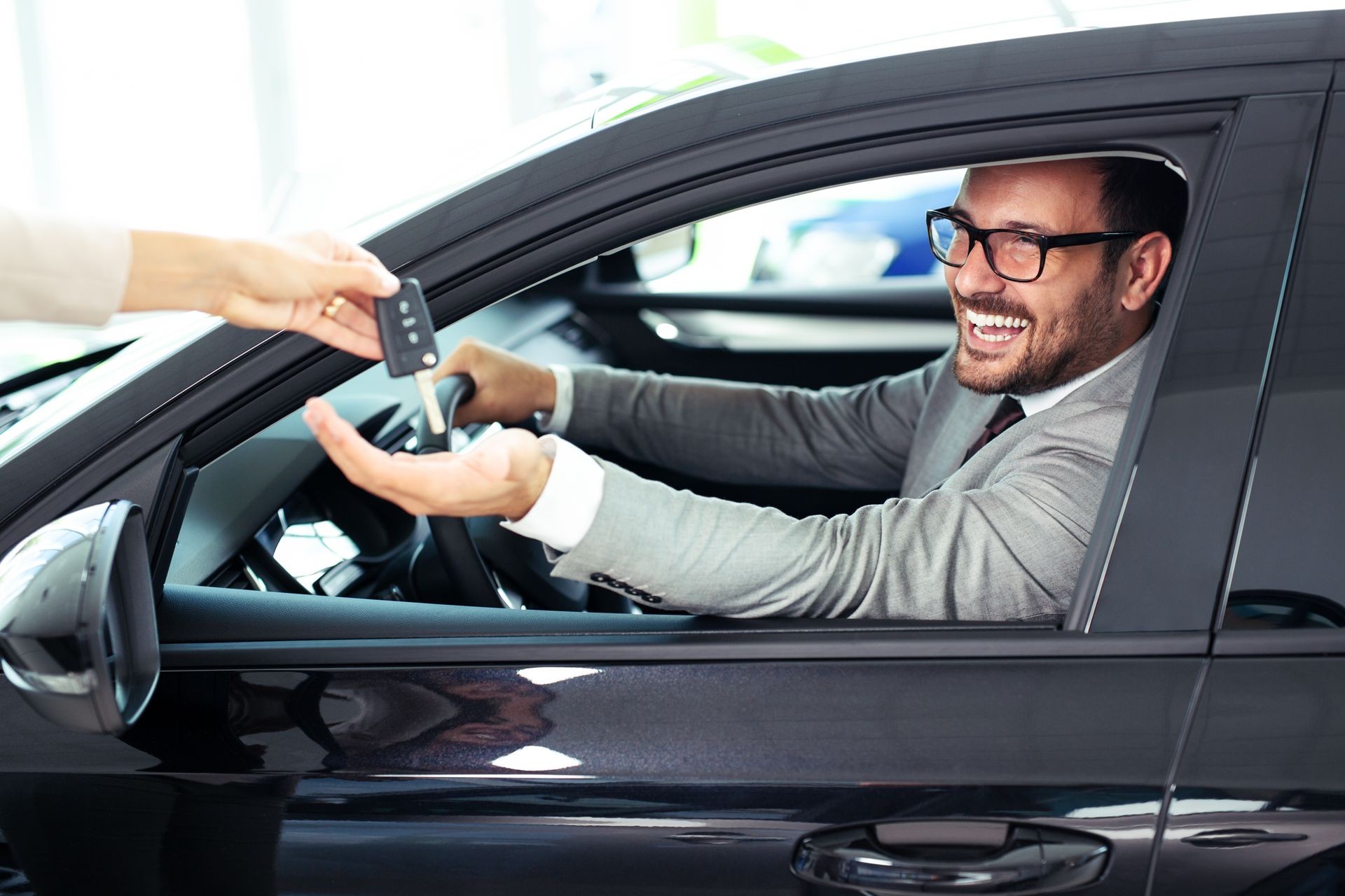 Salesperson during work with customer at car dealership. Giving keys to new car owner.